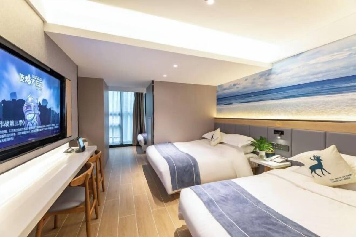 Camera d'albergo con due letti, una TV, una scrivania e un quadro raffigurante una spiaggia.