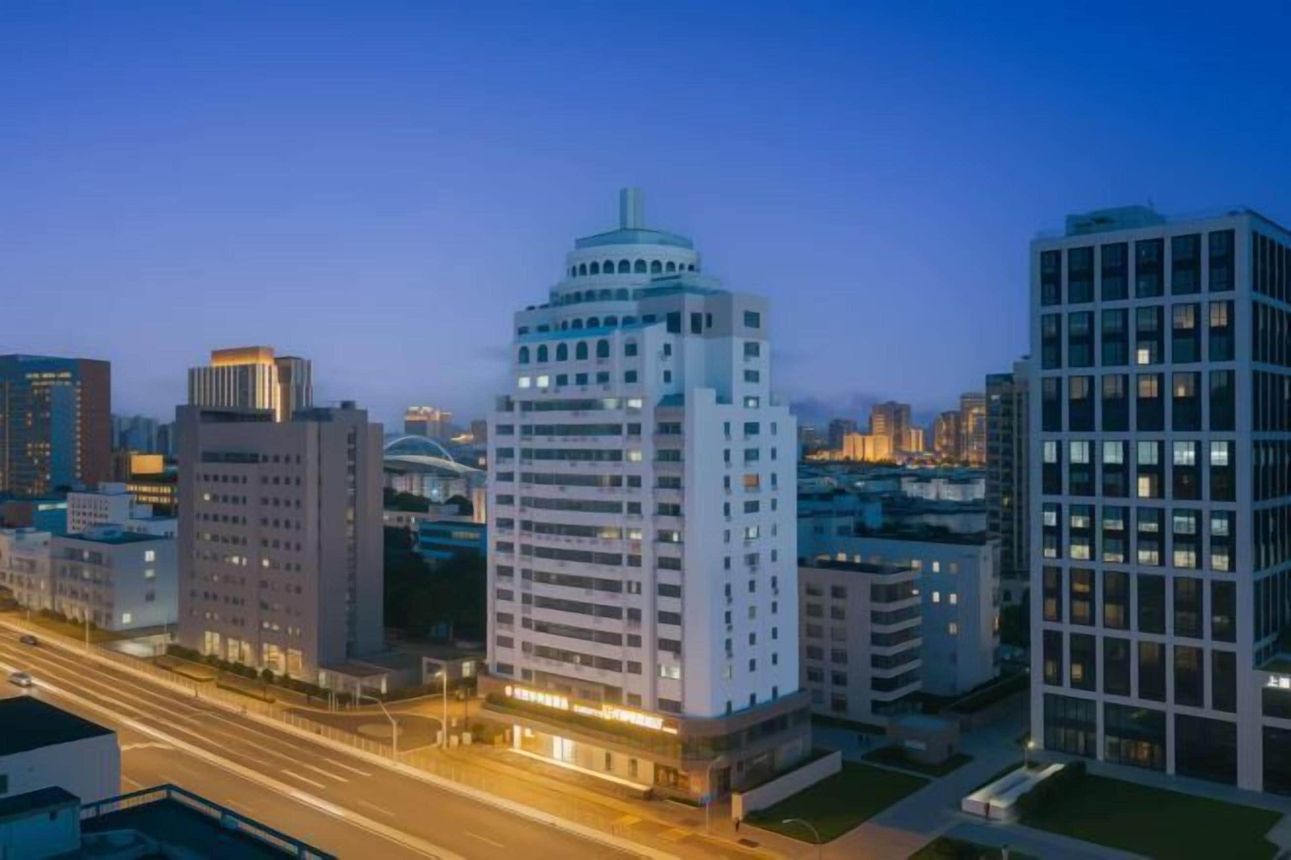 A cityscape at dusk with modern buildings, a prominent dome-shaped structure, and a well-lit street.