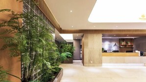Una moderna zona de recepción con mostrador, plantas de interior y un techo alto con iluminación empotrada.