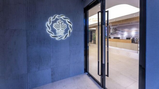 Entrada de un hotel con un logotipo moderno en la pared y un área de recepción visible a través de las puertas de vidrio.