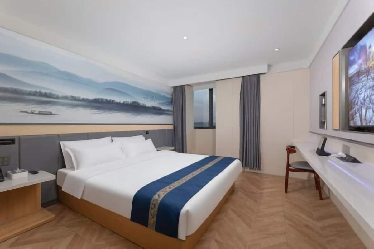 Una camera d'albergo con un letto grande, una scrivania con una sedia, una televisione e un quadro appeso al muro.