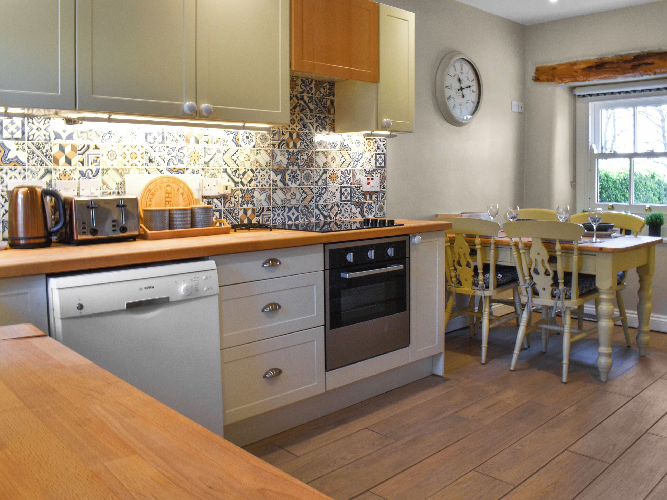 A kitchen with a Bosch dishwasher, an oven, a wooden countertop, and a dining area with yellow chairs.