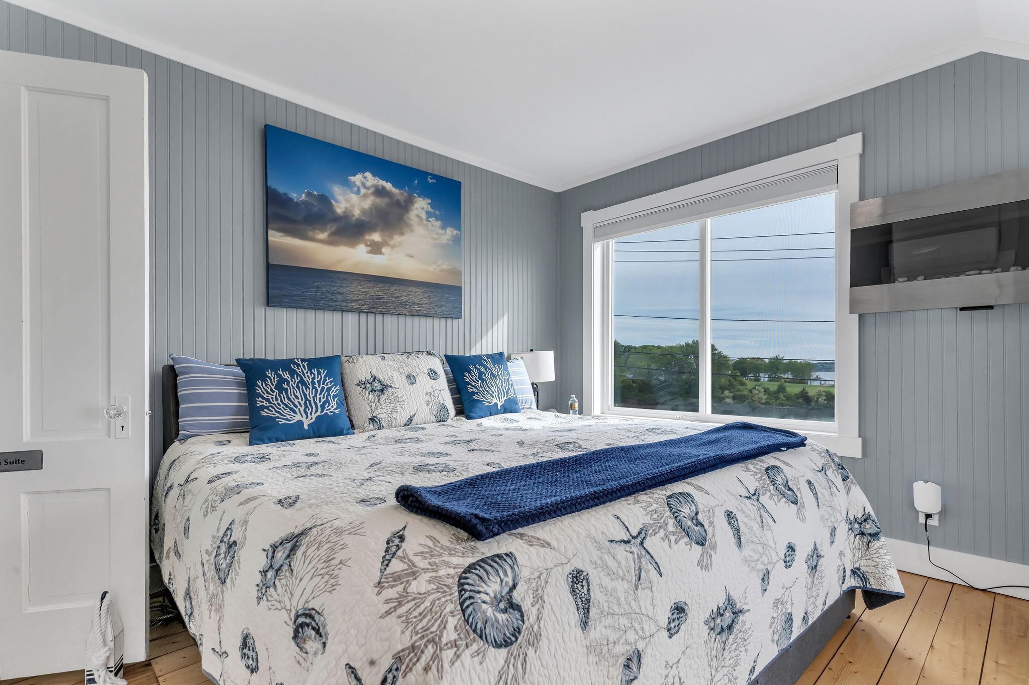 A bedroom with a large bed, a view of the sea, and a painting of a sunset.