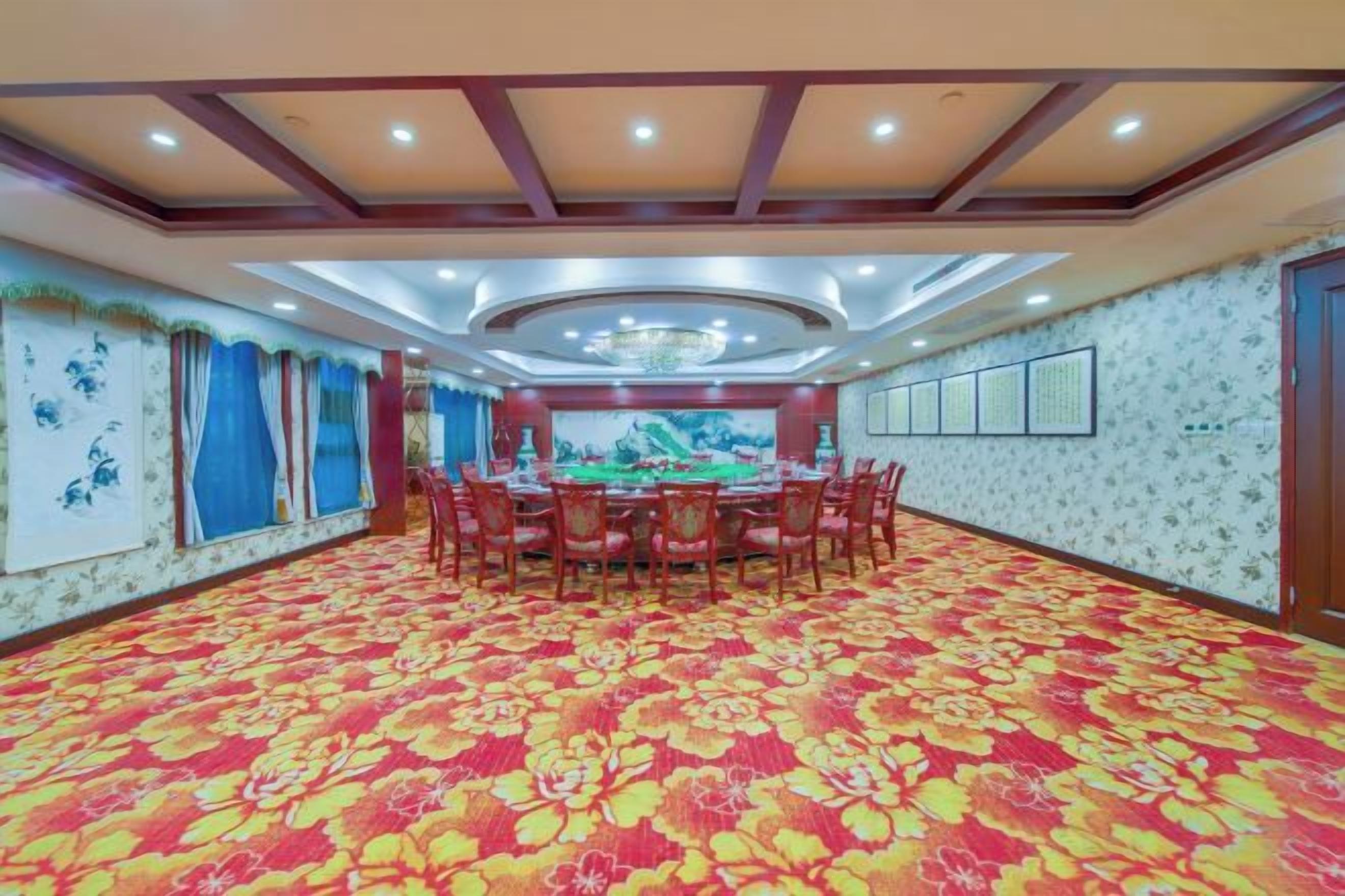 Un salón de banquetes con una gran mesa redonda rodeada de sillas, una alfombra estampada y un techo decorativo.