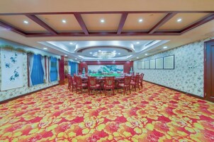 Un salón de banquetes con una gran mesa redonda rodeada de sillas, una alfombra estampada y un techo decorativo.