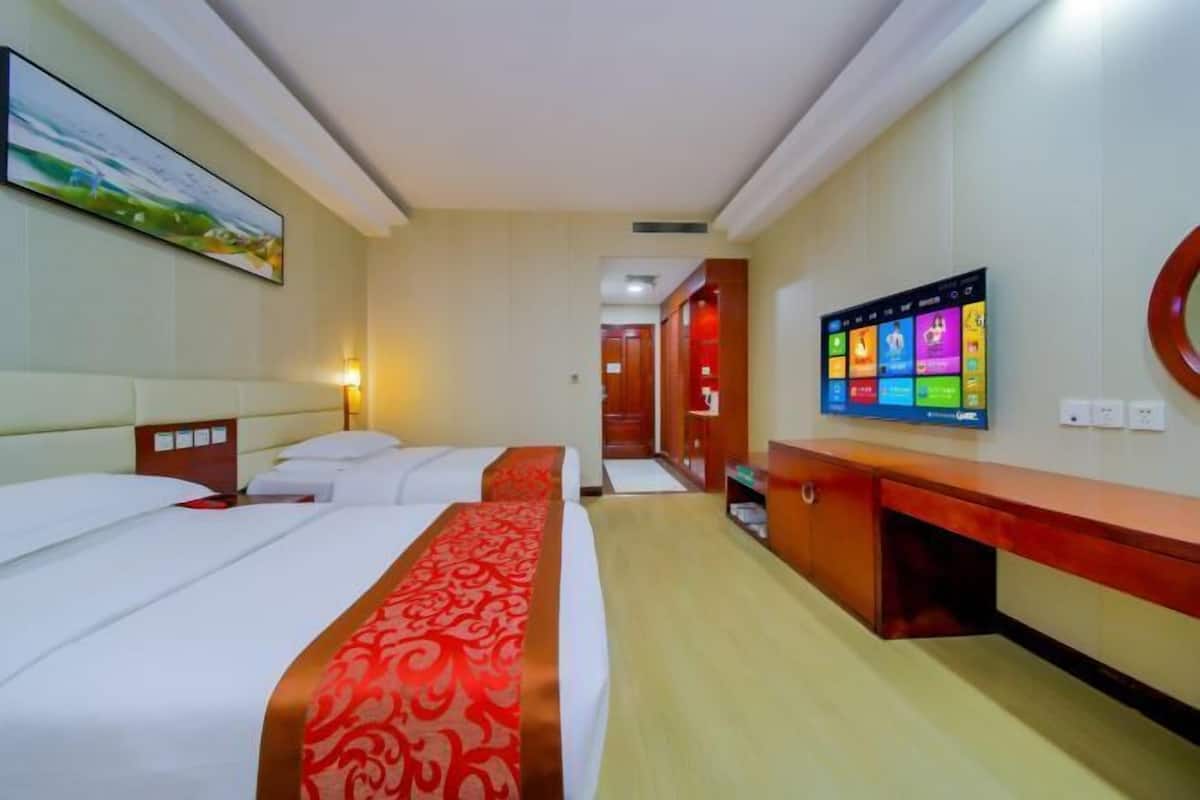 Una camera d'albergo con due letti, una TV a parete e una scrivania in legno.