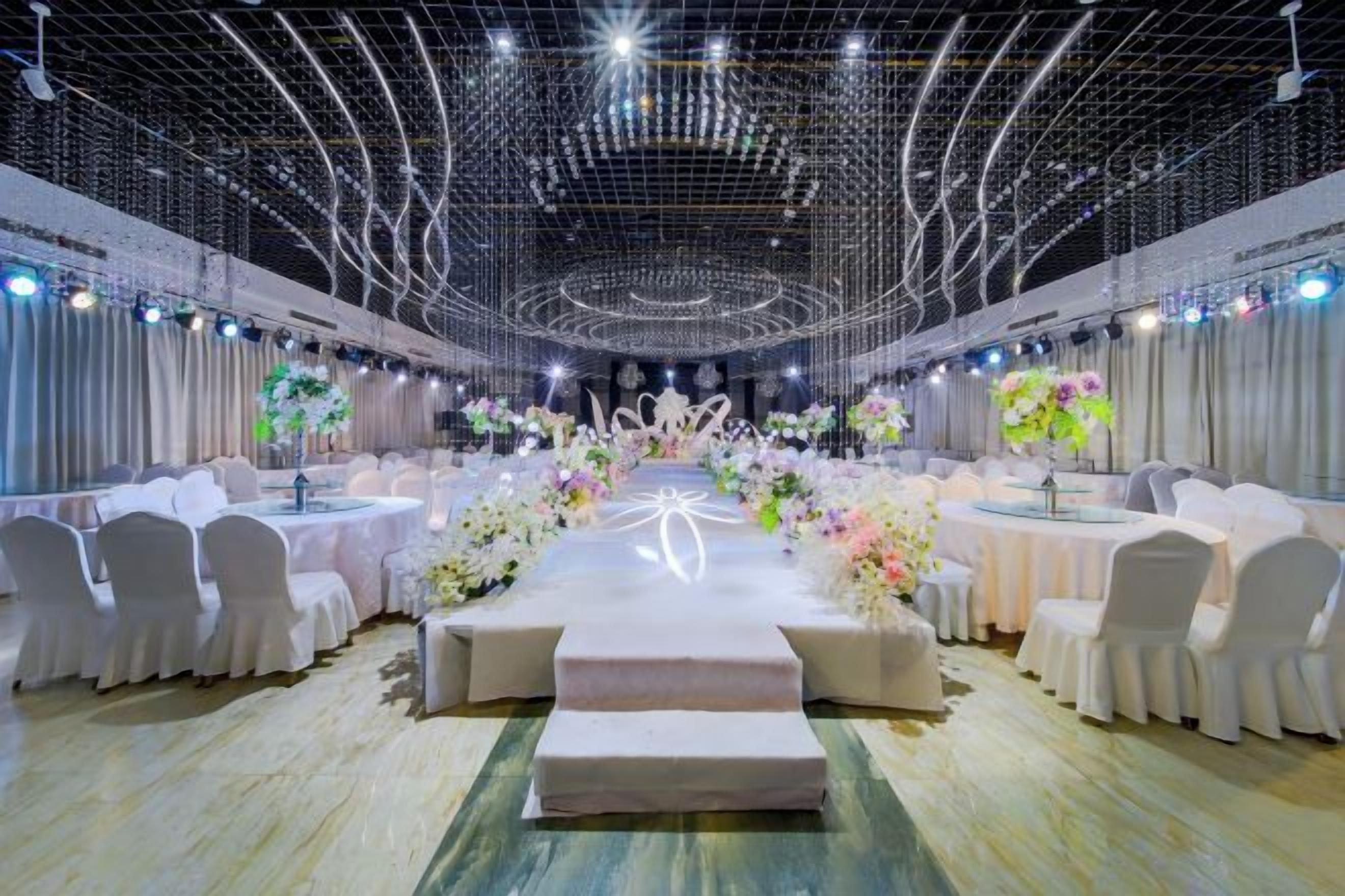 A banquet hall with round tables, white chairs, and floral centerpieces.