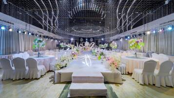 A banquet hall with round tables, white chairs, and floral centerpieces.