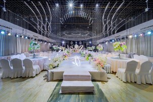 Un salón de banquetes con mesas redondas, sillas blancas y centros de mesa florales.