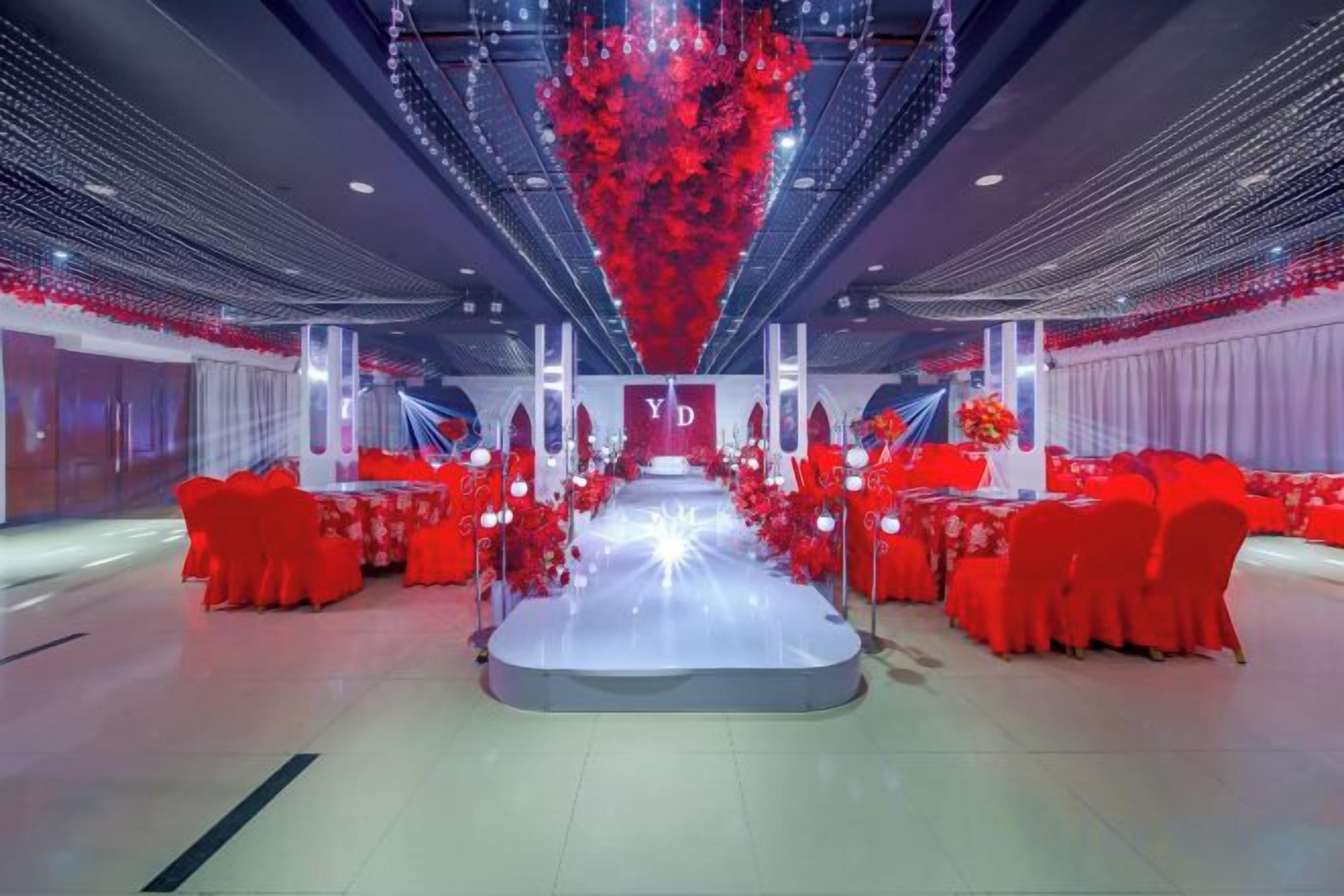 Un amplio salón con un escenario central, sillas rojas y mesas dispuestas para un evento.