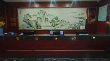 A reception desk with a large traditional painting above it, a digital display, and a marble floor.