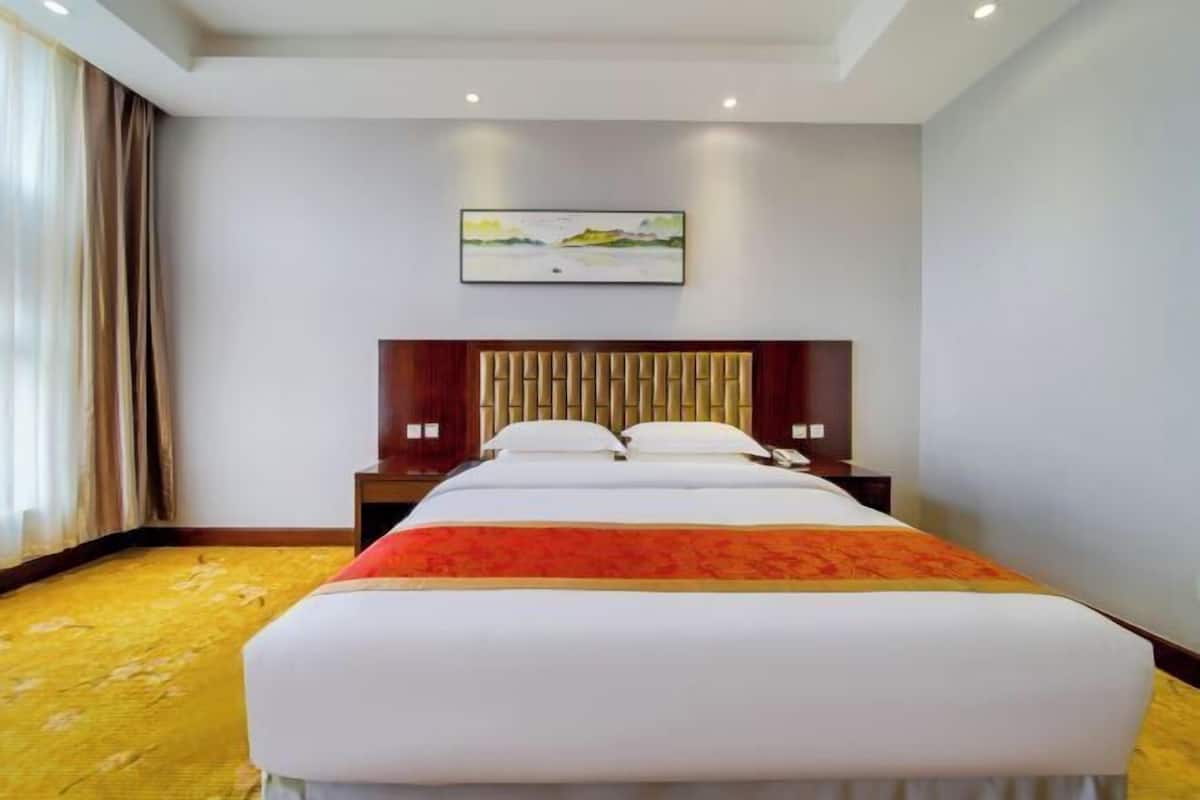 Una camera d'albergo con un letto grande, una testiera, un comodino e un quadro appeso al muro.