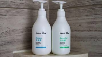 Two bottles of Room Plus shampoo and shower gel on a shelf.