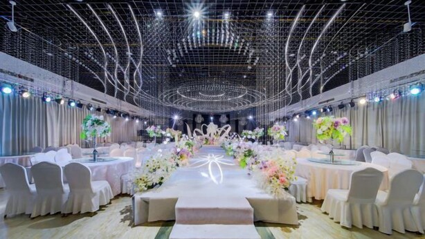 Un salón de banquetes con mesas redondas, sillas blancas y centros de mesa florales.