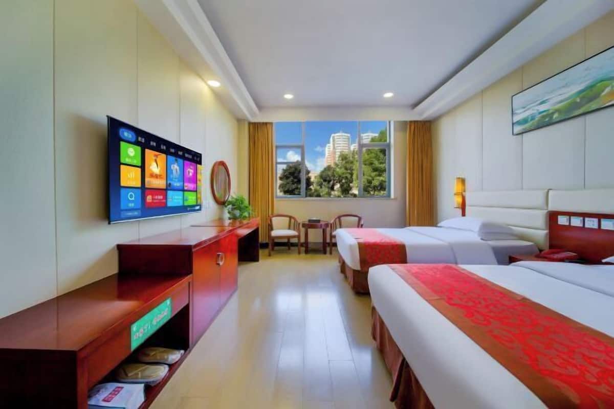 Una camera d'albergo con televisore, scrivania, due letti, una finestra vista città e un quadro appeso al muro.