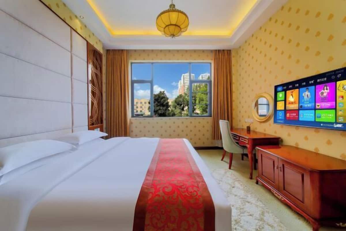 Una camera d'hotel con un letto grande, una scrivania, una televisione e vista sugli edifici dalla finestra.