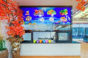 A reception area with a large digital display, a counter, and a potted plant.