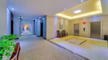 A hotel corridor with a reception desk, elevators, and a seating area with chairs.