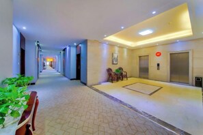 Passadís d'hotel amb una recepció, ascensors i una zona de seients amb cadires.