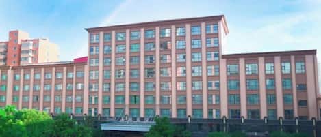 Hotel de varios pisos con entrada central, estacionamiento y zonas verdes circundantes.