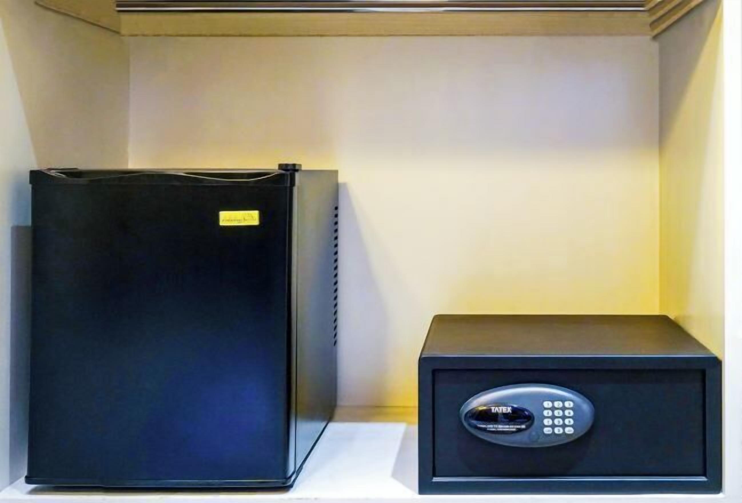 A black safe and a black refrigerator on a white shelf.