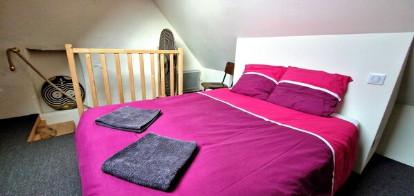 Une chambre à coucher comprenant un lit, des oreillers, une tête de lit en bois, une petite chaise, un radiateur mobile et un radiateur fixé au mur.