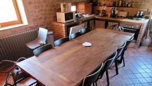 A rustic kitchen with a wooden table and chairs, a window, and stone walls. - Oyé's house (Oyé)