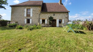 A stone house with a tiled roof, a front door, and a small garden area with a table and chairs. - Oyé's house (Oyé)