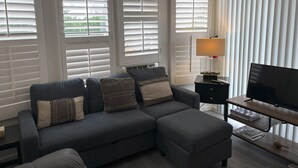A living room with a grey sectional sofa, a TV on a wooden stand, and a lamp on a side table. - Cozy 1-bedroom mobile home with AC, WiFi in tranquil Desert Hot Springs (Desert Hot Springs)