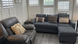 A living room with a grey sectional sofa, a small black side table, and a framed picture on the wall. - Cozy 1-bedroom mobile home with AC, WiFi in tranquil Desert Hot Springs (Desert Hot Springs)