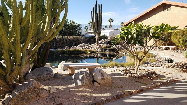 A desert landscape with a pond, large cacti, a stone bench, and a building in the background. - Cozy 1-bedroom mobile home with AC, WiFi in tranquil Desert Hot Springs (Desert Hot Springs)