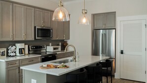 Une cuisine moderne dotée d’un îlot central, d’appareils électroménagers en acier inoxydable et de luminaires suspendus.