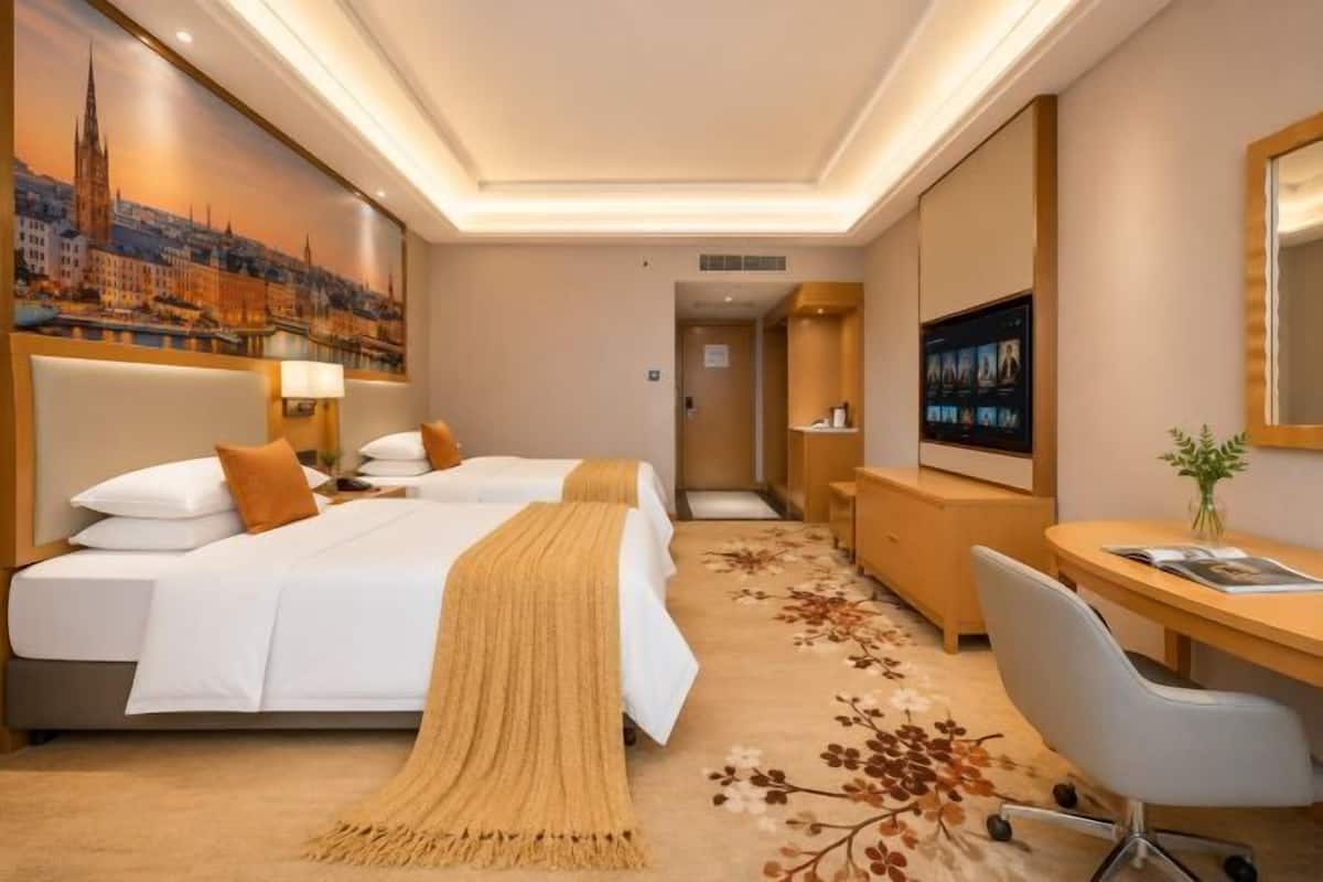 Hotellihuone, jossa on kaksi sänkyä, työpöytä, tuoli, televisio ja kaupunkimaisemaa esittävä taulu.