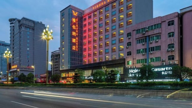 A multi-story Vienna Hotel building with illuminated signage, surrounded by other commercial buildings and street lights. - Vienna Hotel （Dongguan Changping South Station Baihua Times Square Hotel  ） (Dongguan)