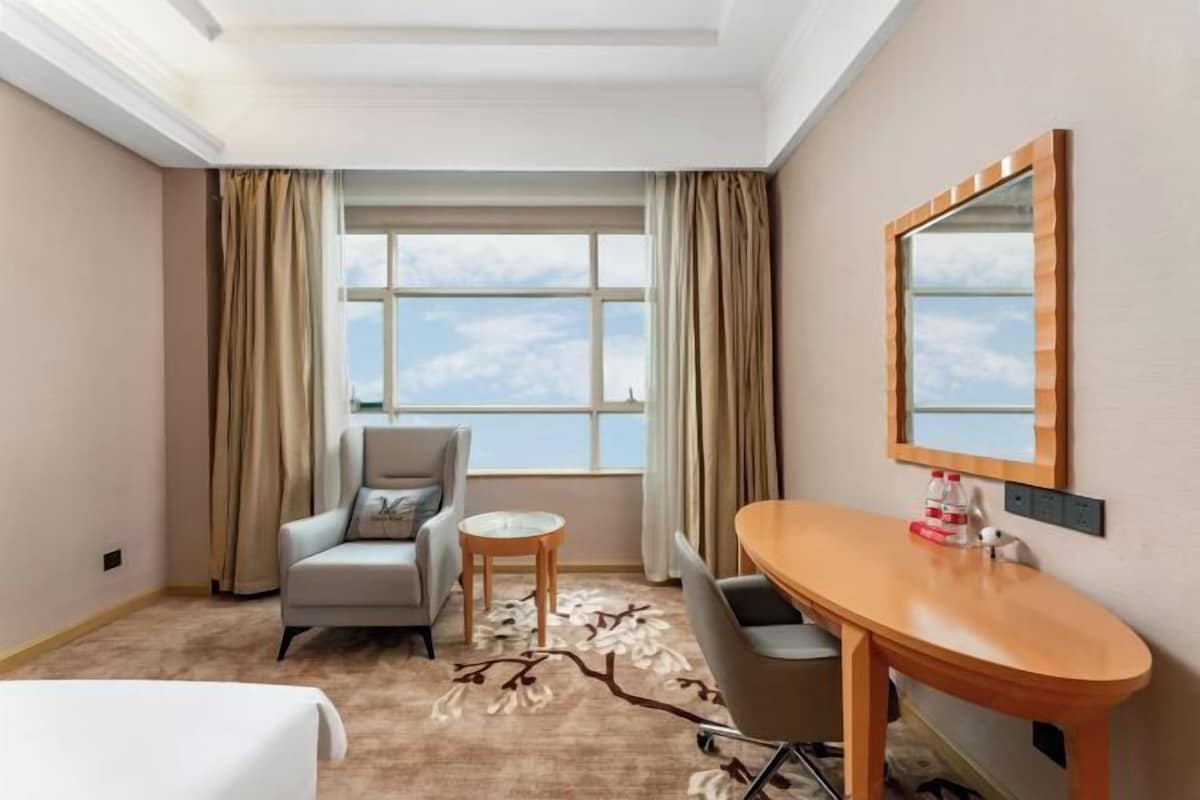 A hotel room with a bed, a desk, a chair, a round table, and a large window with curtains.