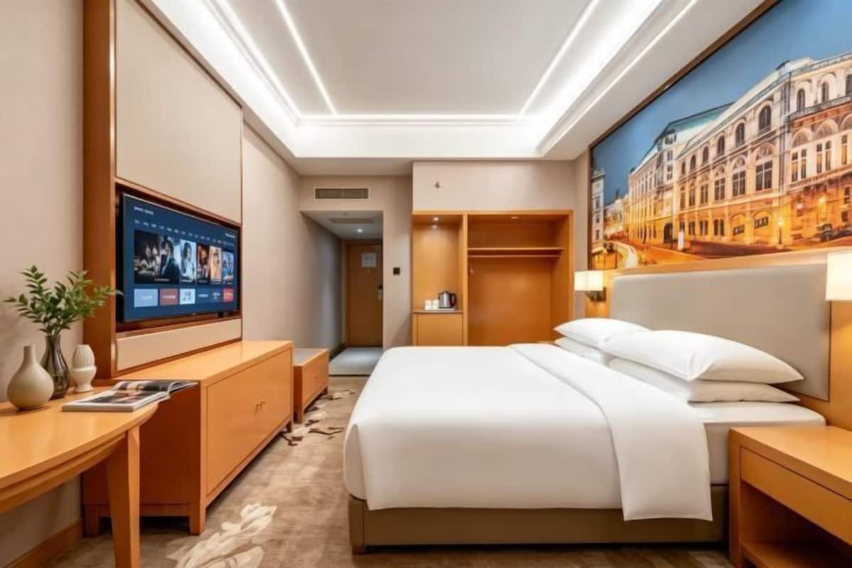 Hotellihuone, jossa on sänky, televisio, työpöytä ja vaatekaappi.