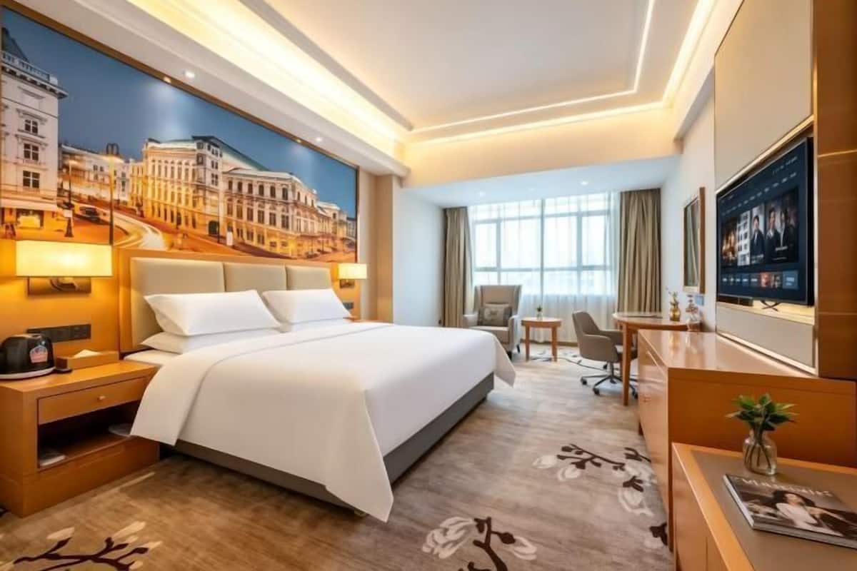 Hotellihuone, jossa on sänky, työpöytä, tuoli, televisio ja taulu seinällä.
