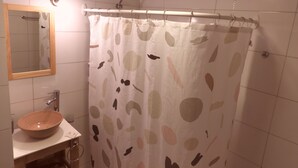 Un baño con cortina de ducha estampada con hojas, un espejo con marco de madera y un lavabo redondo con lavamanos integrado.