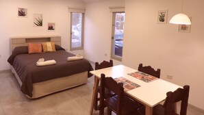 Un dormitorio con cama, una mesa y sillas. Hay ventanas y una lámpara en el techo.