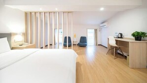 A modern hotel room with a bed, desk, chairs, and a partition.