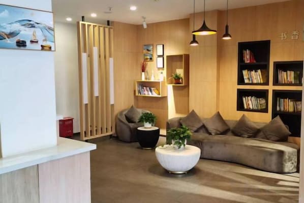 A modern reception area with a reception desk, seating area with sofas, and bookshelves. - Gemeng Hotel (Shanghai Huinan Pazhou Commercial Plaza) (Shanghai)
