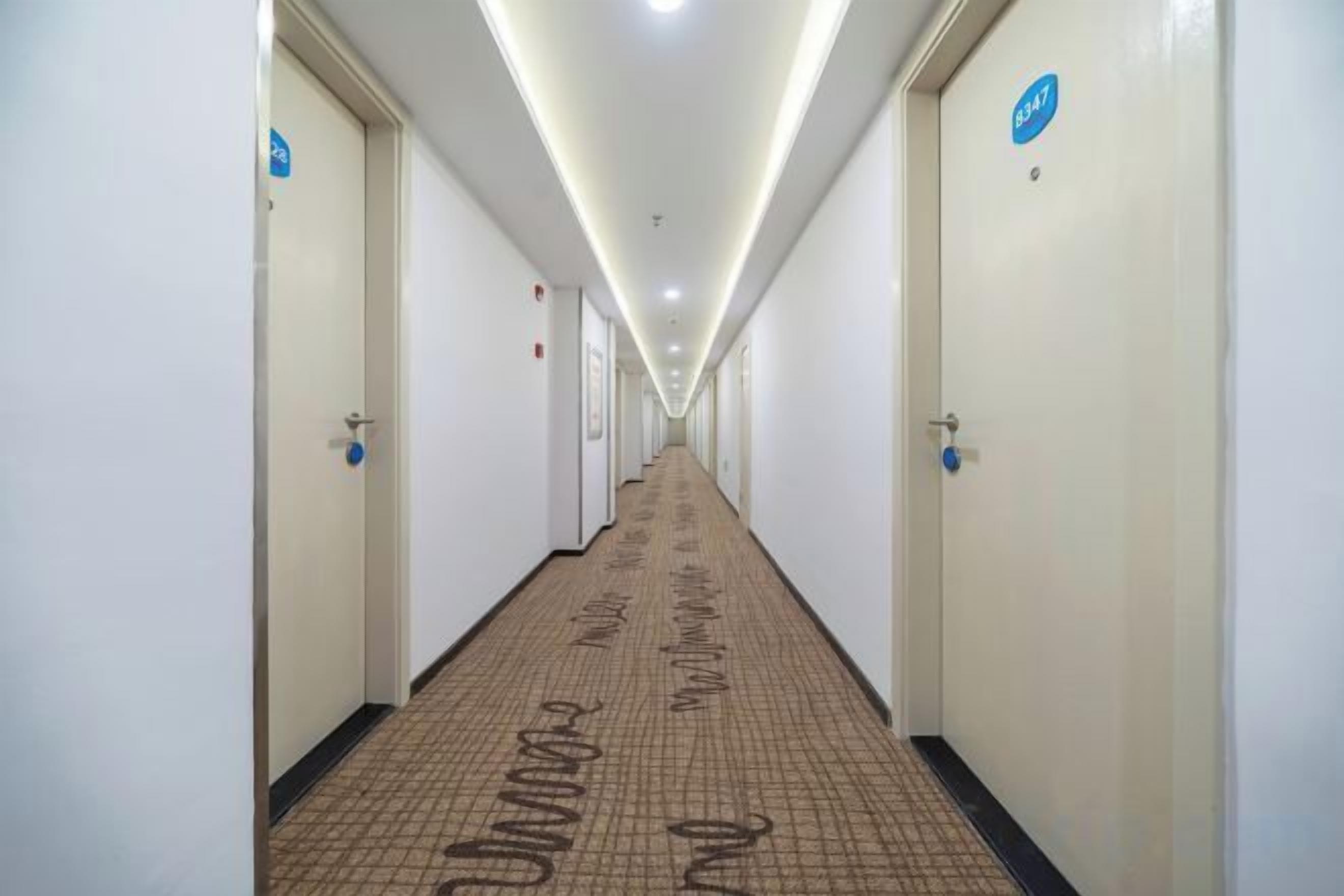 A long, narrow hotel corridor with doors on both sides, marked with directional signs.