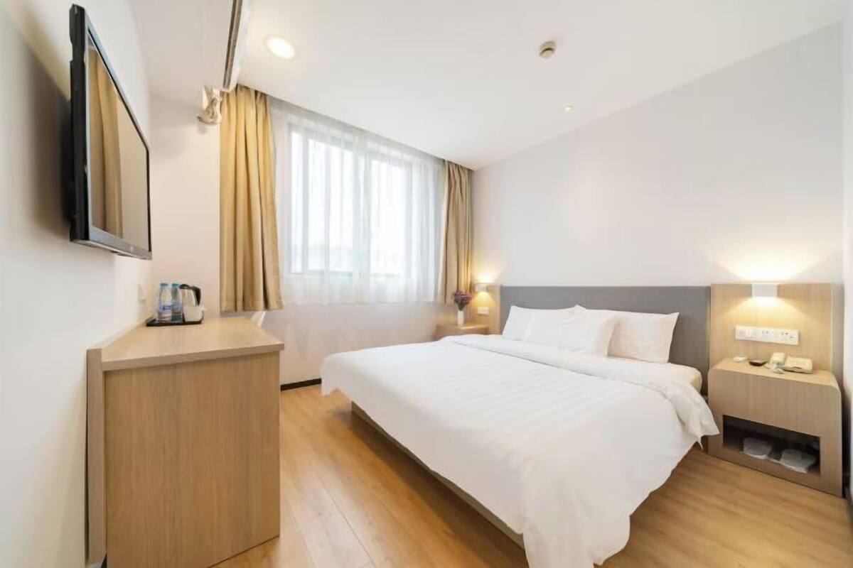 A hotel room with a bed, bedside table, lamp, and a TV mounted on the wall.
