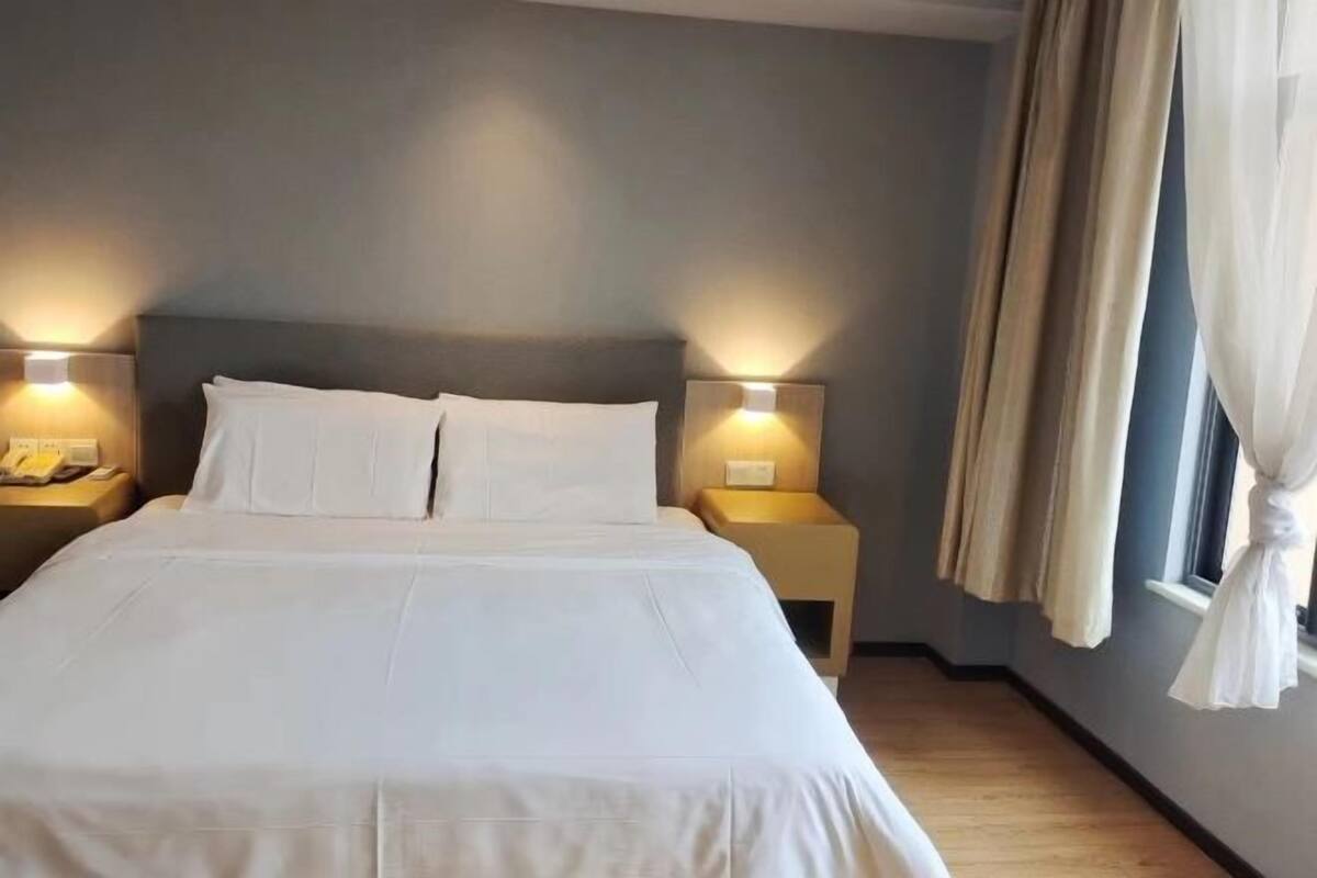 A hotel room with a bed, two bedside tables, and a window with curtains.