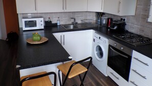A compact kitchen with white cabinets, a microwave, a stove, and a washing machine. - Chelsea Orange Apartment Sleeps10-petsok-parking (London)