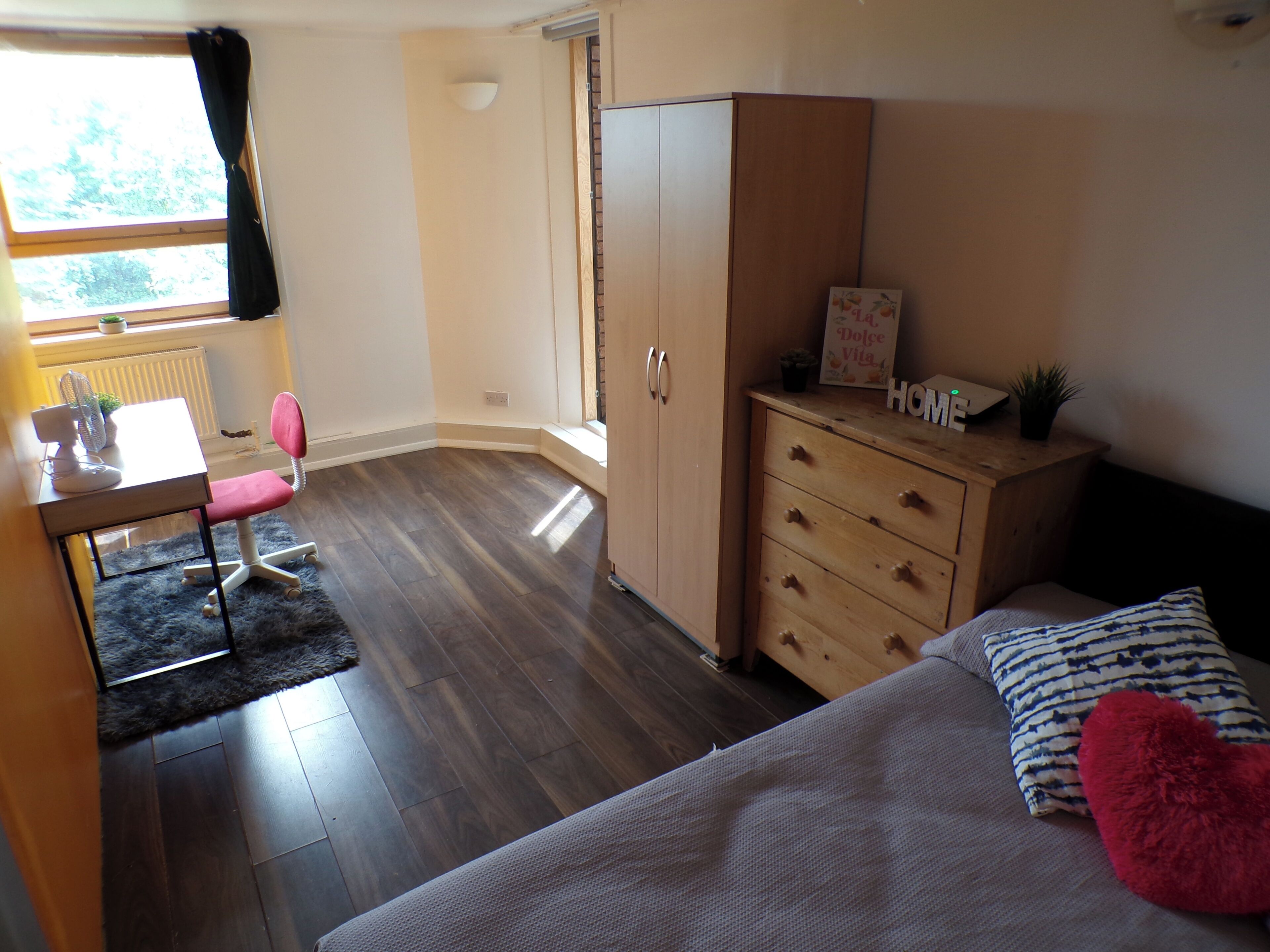 Un dormitorio con cama, escritorio con silla, armario y cómoda.