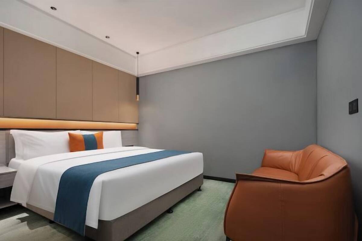 Une chambre d’hôtel moderne équipée d’un lit, d’une table de chevet, d’une chaise et d’une grande fenêtre.