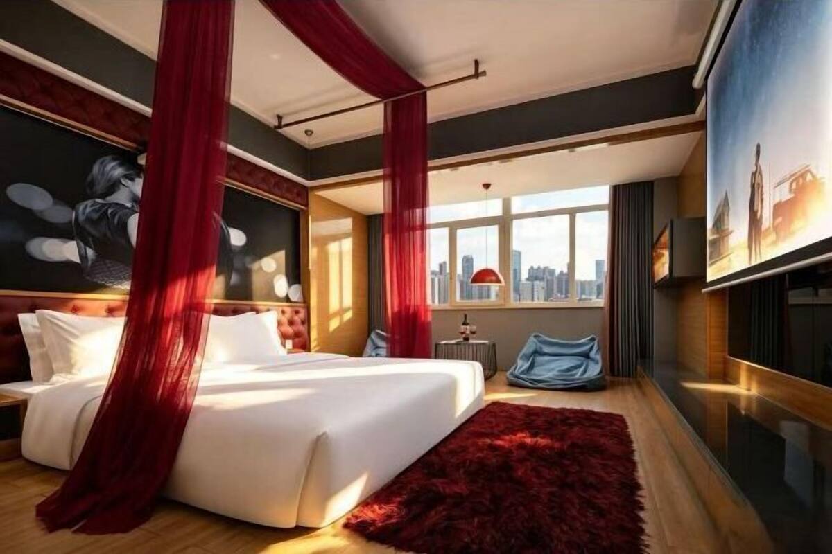 Une chambre d’hôtel moderne avec un grand lit, des rideaux rouges, une vue sur la ville et un tapis rouge.