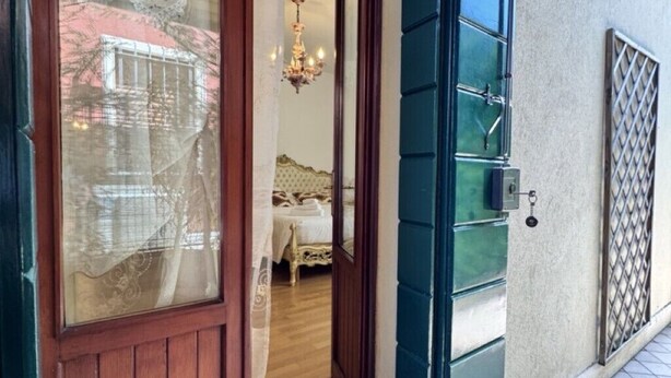 Una puerta de madera con un panel de vidrio y un marco verde que da a un dormitorio con una cama y una araña.