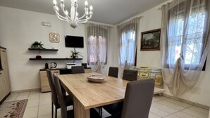 Un comedor con una mesa y sillas de madera, una araña y una cocina al fondo.